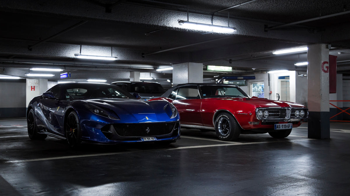Two luxury sports cars parked in a dimly lit urban parking garage, showcasing sleek designs.