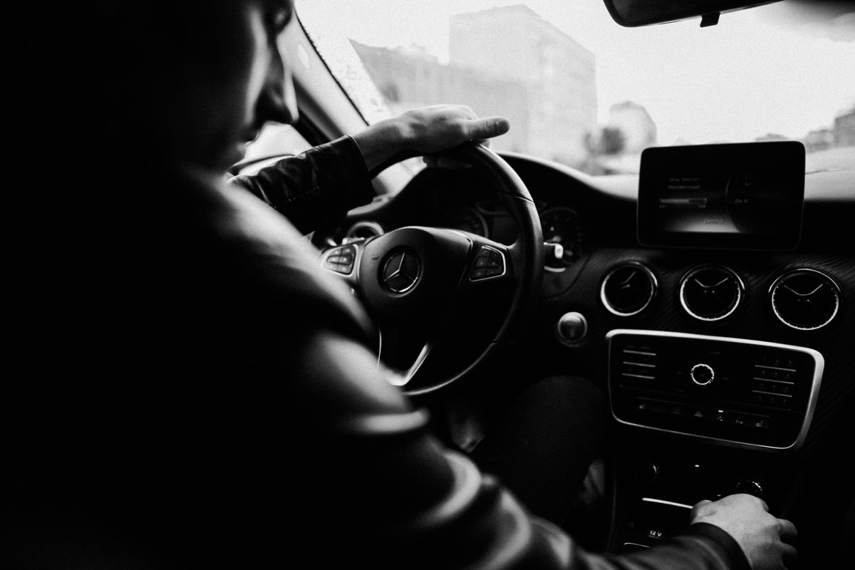 Black and white photo showcasing a man driving a luxury car, focusing on the interior details.